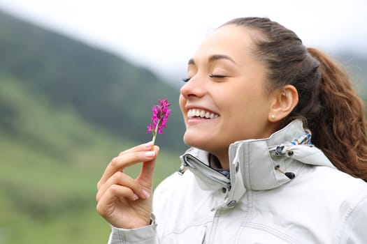 Happy hiker smelling wild flower standing in nature