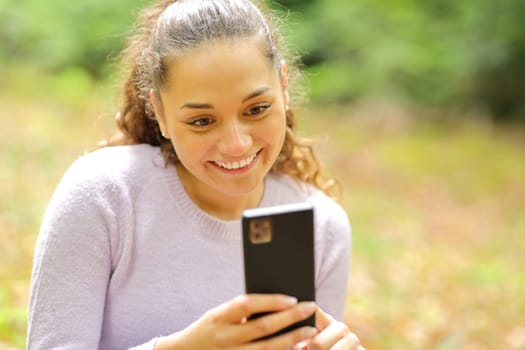 Happy woman sitting in a forest or park using smart phone