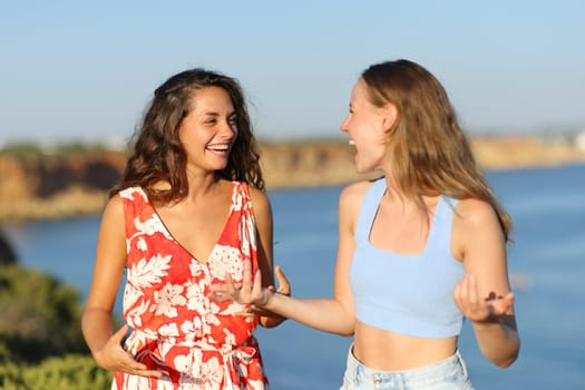Two happy friends on summer holidays talking on the beach
