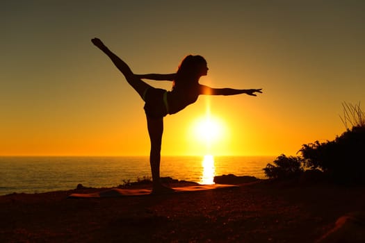 Profile of a backlight ballerina silhouette stretching dancing ballet at sunset on the beach