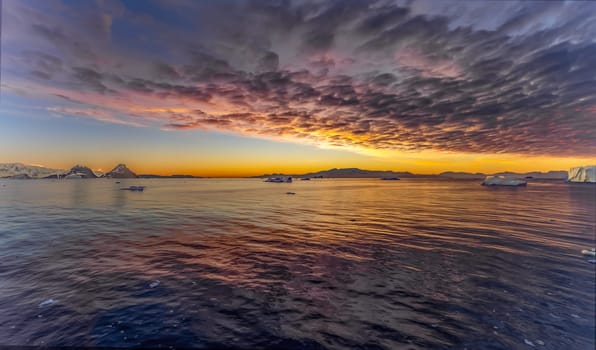 Cruise ship sails through wintry Cierva Cove - a deep inlet on the west side of the Antarctic Peninsula, ringed by Cierva Bay in San Martín Land - Antarctica, during a dramatic sunset / evening sunset.