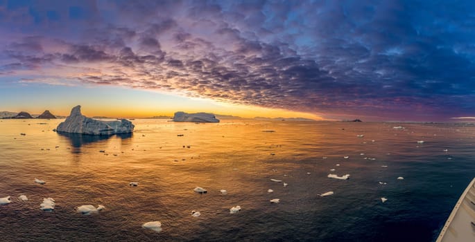 Cruise ship sails through wintry Cierva Cove - a deep inlet on the west side of the Antarctic Peninsula, ringed by Cierva Bay in San Martín Land - Antarctica, during a dramatic sunset / evening sunset.