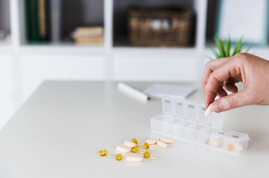 Closeup of female elderly hands sorting, organizing pills. Medical pill box with doses of tablets for daily take with white, yellow, beige drugs, capsules. Young woman get her daily vitamins at home