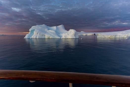 Cruise ship sails through wintry Cierva Cove - a deep inlet on the west side of the Antarctic Peninsula, ringed by Cierva Bay in San Martín Land - Antarctica, during a dramatic sunset / evening sunset.