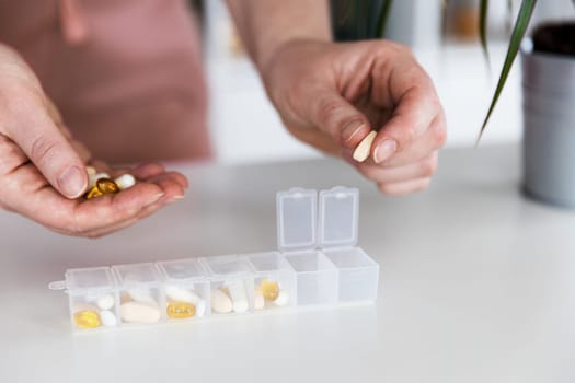 Female hands sorting pills. Young woman getting her daily vitamins at home. Closeup of medical pill box with doses of tablets for daily take a medicine with different white, yellow drugs and capsules