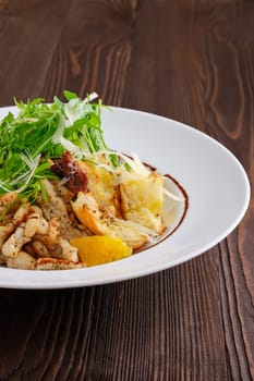 Closeup view of salad with fried chicken meat, dried tomato, cashew nuts and orange balsamic sauce served with arugula and parmesan on dark wooden background