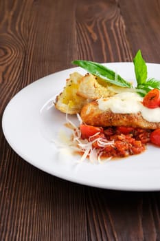 Closeup view of roasted chicken fillet with tomato cherry, parmesan and crouton on dark wooden background