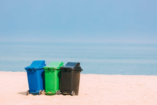 Three Plastic Waste Containers On Wheels For Separate Collection Of Garbage. Containers For Temporarily Storing Waste. Dustbins, Garbage Cans, Trash Cans On Sea Ocean Coast Beach.