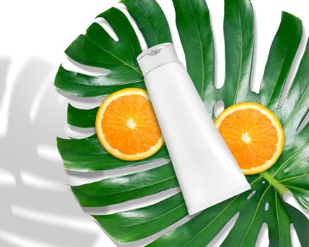 Luxury skin care product ad, top view of blank packaging cosmetic plastic tube with monstera leaf and oranges
