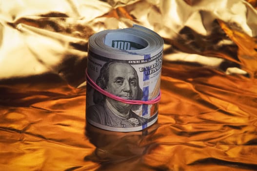 A roll of one hundred American dollars in close-up on a gold background. A big pile of cash dollars. One hundred dollar bills. Close-up, free space for captions and text.