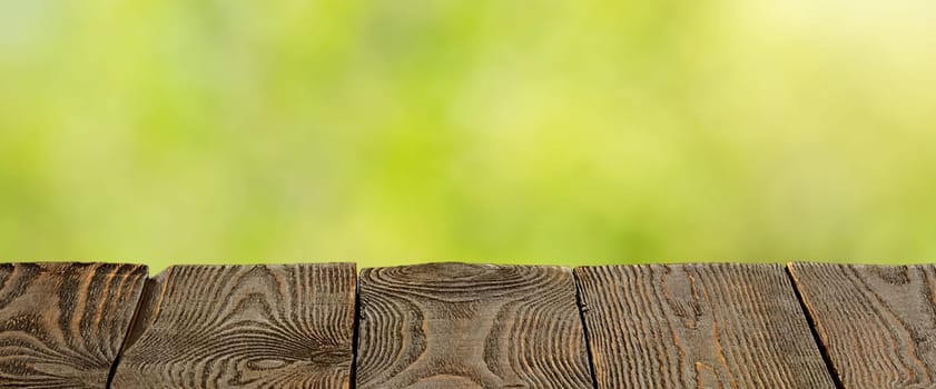 Background with blurred green leaves and empty wooden planks in the foreground. For product demonstrations, free space, layout, mockup, perspective board, background board.