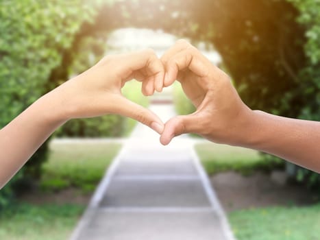couple making heart shape with hands in park