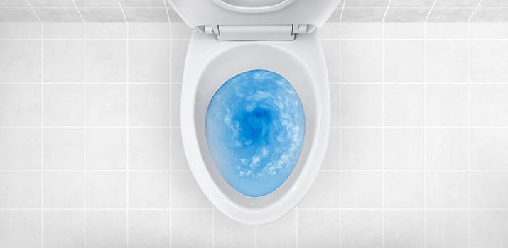 Top view of toilet bowl, blue detergent flushing in it