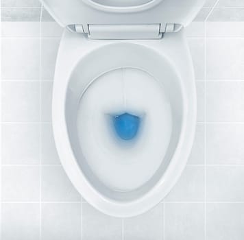 Top view of toilet bowl, blue detergent flushing in it