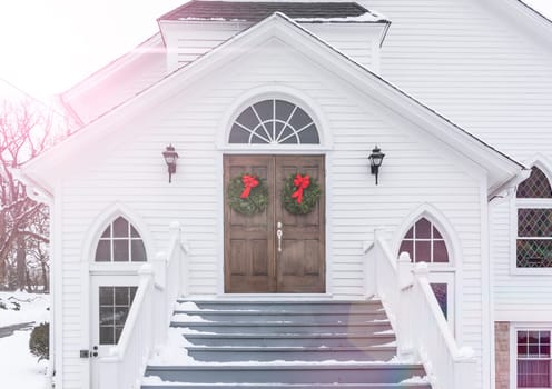 Christmas Wreaths Hang from Entrance Doors of Rustic Church In Winter Snow Scene.