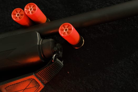 shell magazine into the barrel of a long shotgun on dark background with leather belt.