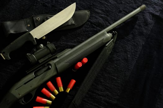 Weapon on black cloth: knife, rifle, shells,top view. Top view of knife, rifle shells