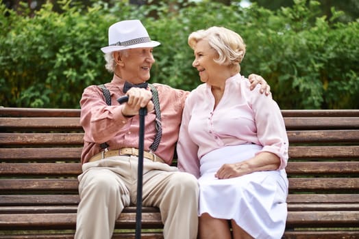 Happy senior couple sitting on bench in park and talking