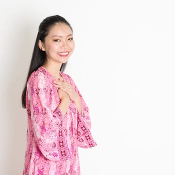Portrait of happy Southeast Asian girl in pink batik dress standing on plain background.
