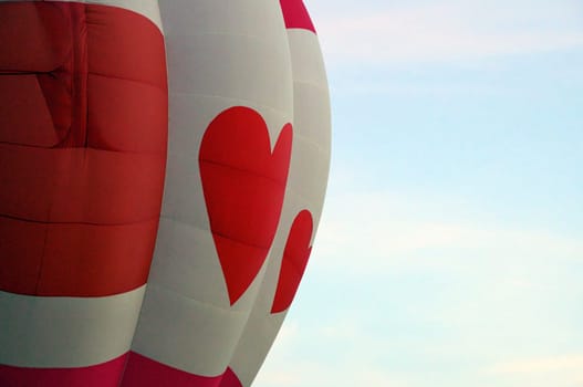Close up of a red and white hot air balloon with hearts against the morning sky.