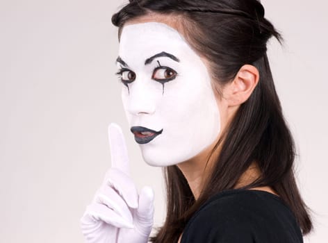Woman made up in white face frames mouth with index finger