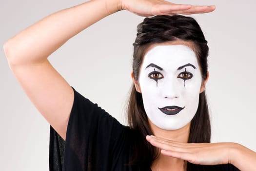 Woman made up in white face frames her features with her hands
