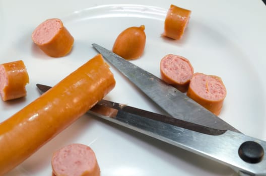 Cut Frankfurt sausages with scissors. Sausage pieces on white plates.