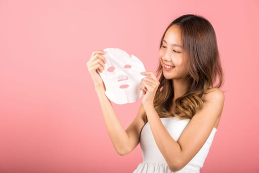 Healthcare spa. Asian woman holding purifying mask face on hands, Portrait beautiful female smiling holds facial sheet mask, Studio shot isolated on blue background, Face care and beauty treatments