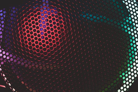 Colorful light of computer fan shines through the holes of protective grid. illumination glows in the dark. abstract futuristic background. led lighting of gaming pc