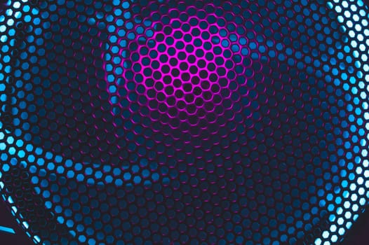 Colorful light of computer fan shines through the holes of protective grid. illumination glows in the dark. abstract futuristic background. led lighting of gaming pc