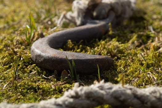 Rusty metal hook with rope lies on the green grass