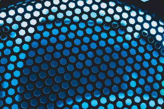 Blue light shines through the ventilation grid holes of computer air cooling system. abstract background