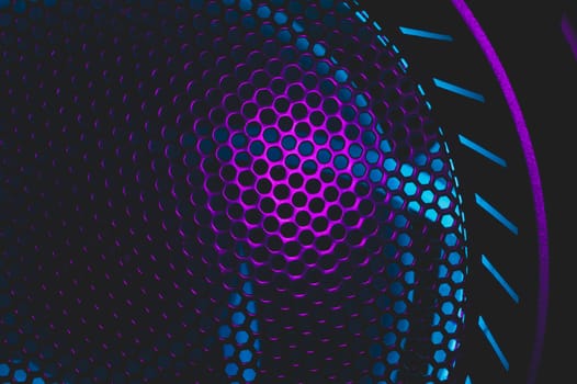 Colorful light of computer fan shines through the holes of protective grid. illumination glows in the dark. abstract futuristic background. led lighting of gaming pc