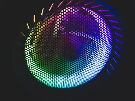 Colorful led lights of computer fan shines through the protective grid. illumination glows in the dark. abstract futuristic background