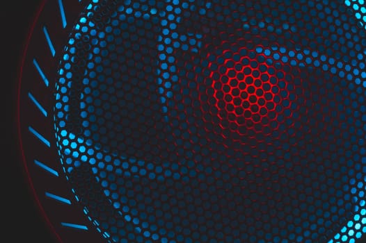 Colorful light of computer fan shines through the holes of protective grid. illumination glows in the dark. abstract futuristic background. led lighting of gaming pc