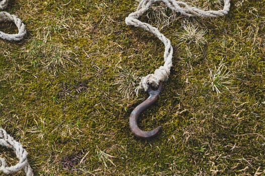 Rusty metal hook with rope lies on the green grass. marine equipment