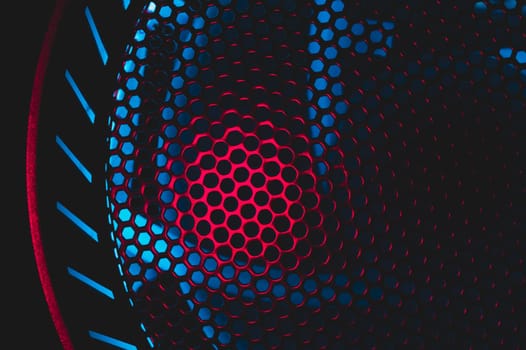 Colorful light of computer fan shines through the holes of protective grid. illumination glows in the dark. abstract futuristic background. led lighting of gaming pc