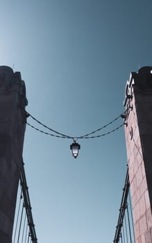 Ancient iron lantern hanging on a chain between stone walls against blue sky