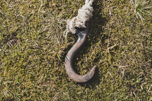 Rusty metal hook with rope lies on the green grass. marine equipment