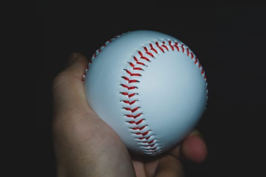 Baseball ball in hand close up on black background