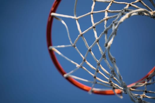 closeup of outdoor basketball basket net of white rope view from underneath against a blue sky with copyspace