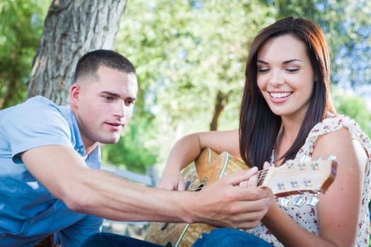 Young Adult Man Teaching Girlfriend How To Play The Guitar Outside in the Park.