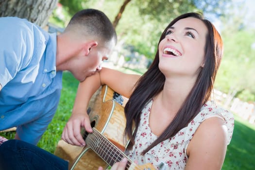 Young Adult Girl Playing Guitar with Boyfriend In The Park.