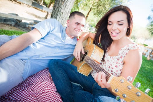 Young Adult Girl Playing Guitar with Boyfriend In The Park.