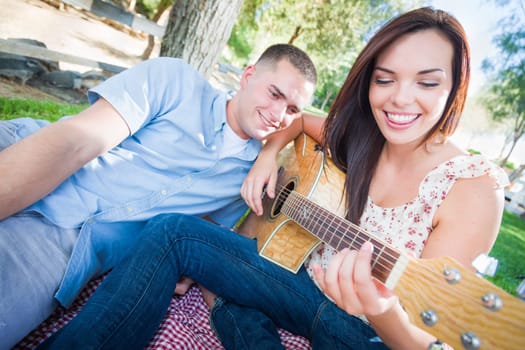 Young Adult Girl Playing Guitar with Boyfriend In The Park.