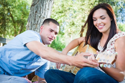 Young Adult Man Teaching Girlfriend How To Play The Guitar Outside in the Park.
