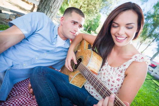 Young Adult Girl Playing Guitar with Boyfriend In The Park.