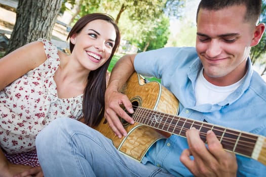 Young Adult Man Playing Guitar for His Girlfriend in the Park.