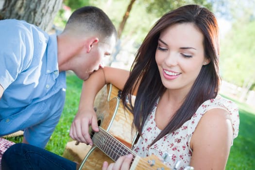 Young Adult Girl Playing Guitar with Boyfriend In The Park.