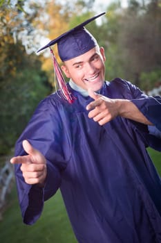 Happy Handsome Male Graduate in Cap and Gown Outside.